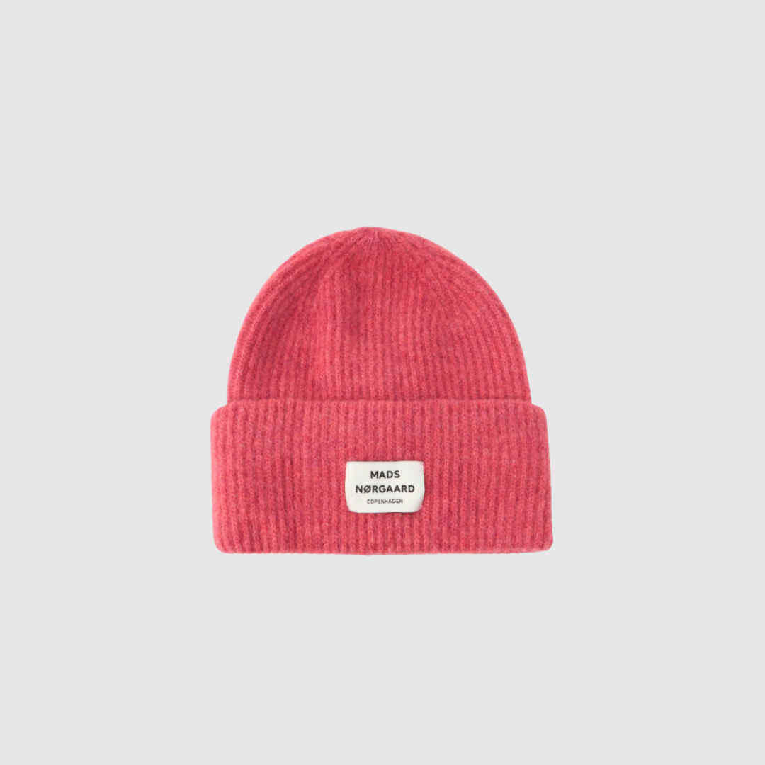 Tosca Anju Hat fra Mads Nørgaard er en moderne og blød ribstrikket hue med bredt ombuk og logolabel foran. Her i en frisk fuchsia pink farve, der tilføjer farve og personlighed til dit vinterlook. Huen er fremstillet i en varm og komfortabel uldblanding og passer perfekt til både hverdag og udendørs aktiviteter. Køb din hue hos Merci Give og få hurtig levering og personlig service.