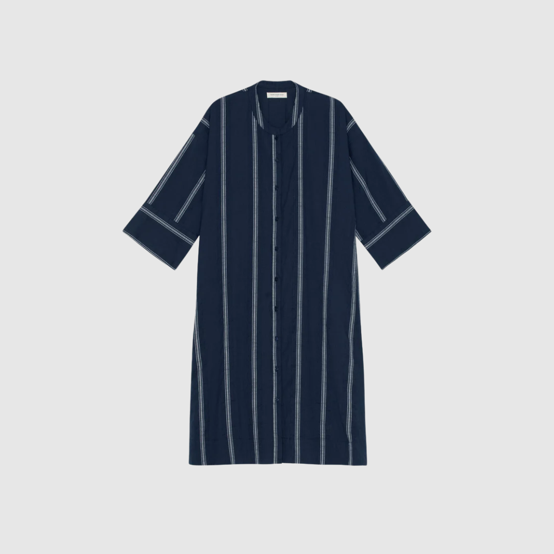 Opdag Lively Shirtdress Stripe fra Moshi Moshi Mind – en let og feminin skjortekjole i certificeret økologisk bomuld. A‑line pasformen, den kinesiske krave, 3/4‑ærmerne og de fine blondedetaljer skaber et elegant og moderne udtryk. Den mørk navy/hvide stribe gør kjolen stilren og klassisk, samtidig med at draperingen giver et smukt, levende fald. En alsidig style, perfekt til både hverdag, ferie og sommersæsonens pænere anledninger.