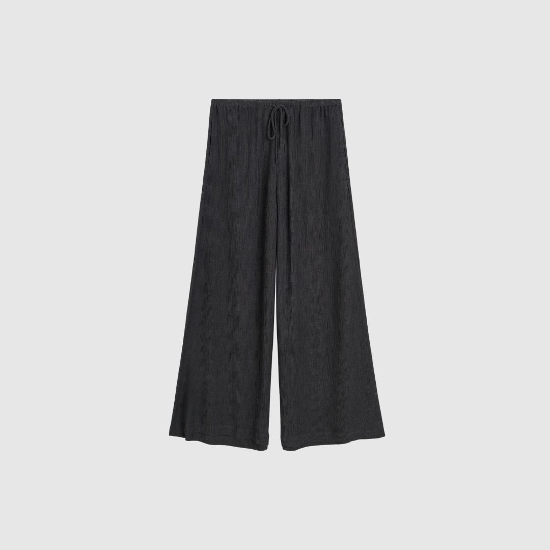 Opdag Pisca Weave Bukser fra By Malene Birger – elegante, luftige bukser med høj elastisk talje og brede ben. De ansvarligt fremstillede ECOVERO™ viskosefibre giver et smukt, naturligt fald, og den sorte farve gør bukserne nemme at style. Perfekt til alt fra afslappede dage til smarte sommerlooks – og ekstra smukke sammen med Rose Weave‑blusen.