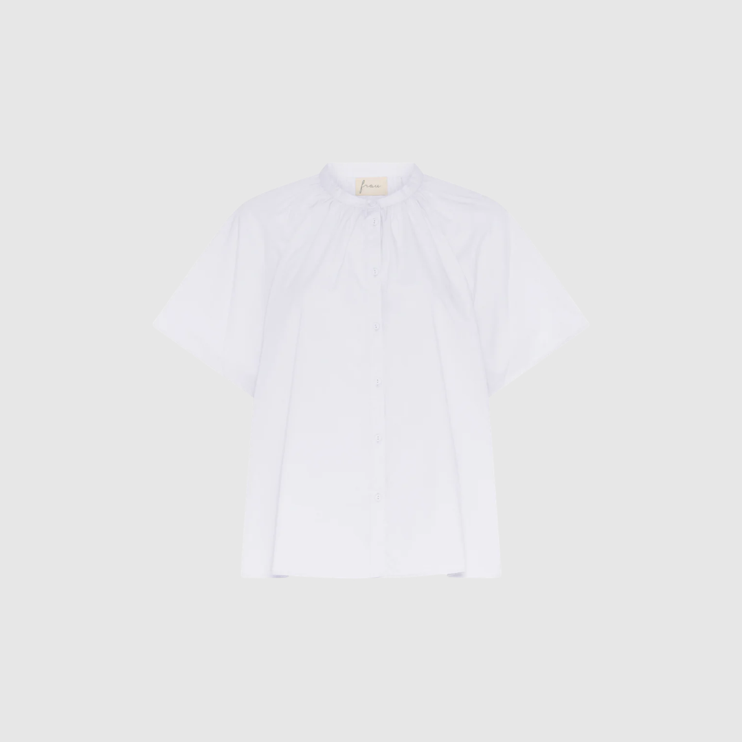 Siena Kortærmet Skjorte – Bright White fra FRAU er en feminin og tidløs skjorte i 100% økologisk bomuld. Med kinakrave, raglanærmer og rynkedetaljer får du en elegant, luftig og let style, der passer til både hverdag, rejse og pæne anledninger.