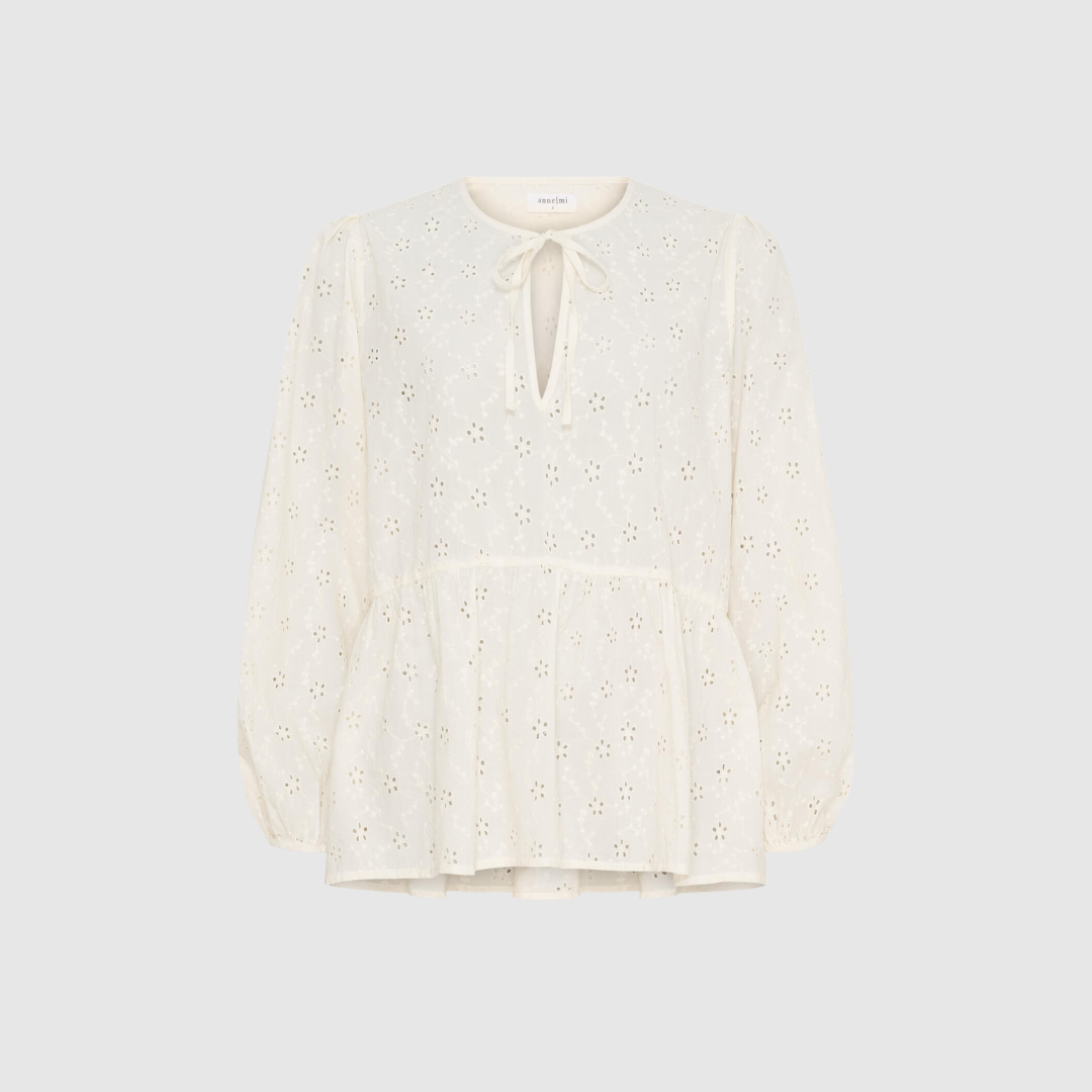Melody LS Blouse i White Sand er en feminin bluse i broderie anglaise med V‑hals, bindebånd og elastiske trompetærmer. Foret med blød bomuld for optimal komfort. Perfekt til både hverdag og mere pyntede anledninger.
